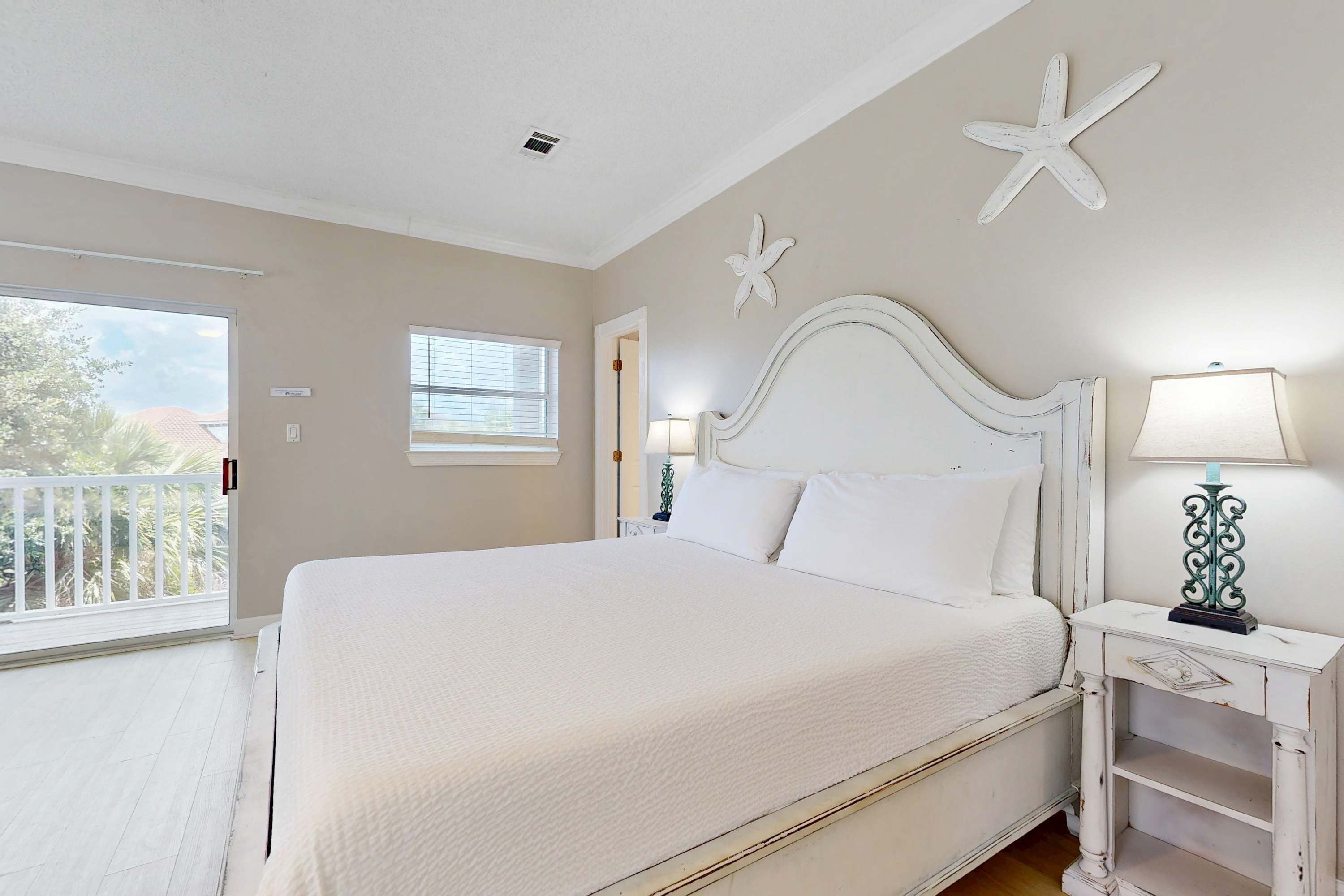 A bedroom with a large bed, a nightstand with a lamp, a starfish decoration on the wall, and a window with blinds.