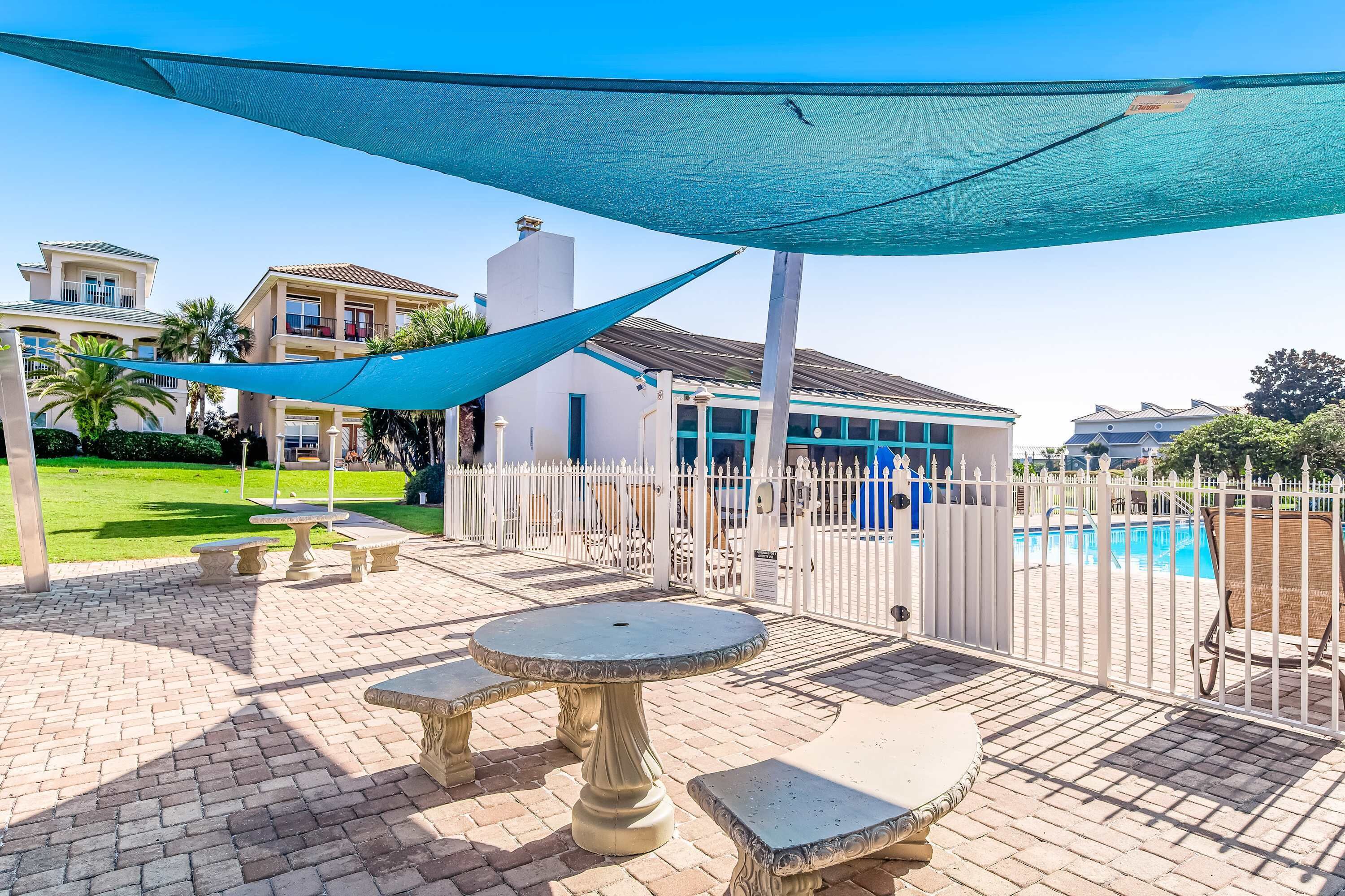 Ein Patio mit Steintischen und -bänken, einem Pool und einem weißen Zaun.