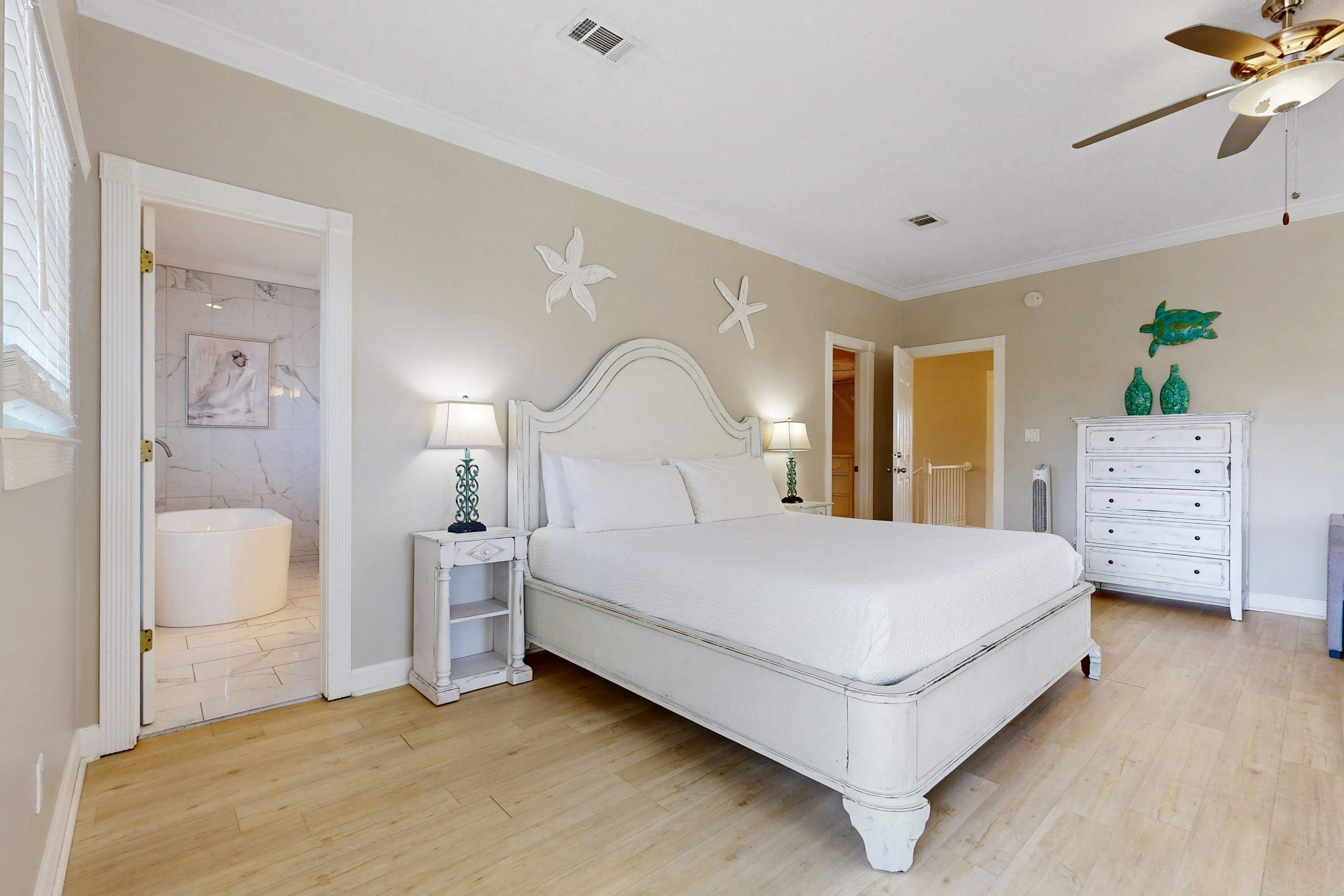 A bedroom with a large bed, bedside tables with lamps, a dresser, and decorative wall art.