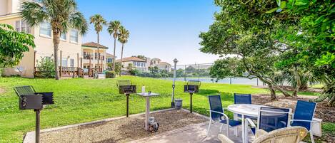 A patio area with outdoor furniture, a grill, and a view of a lake and buildings in the background.