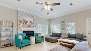 A spacious living room with a fireplace, teal and gray sofas, a wooden coffee table, and a ceiling fan. - Casa Blanca (Destin)