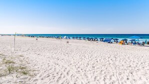 A beach with tents and umbrellas, a clear sky, and the ocean in the background. - Casa Blanca (Destin)