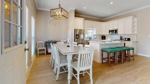 A spacious kitchen with white cabinetry, a central island with stools, and a dining table with chairs. - Casa Blanca (Destin)