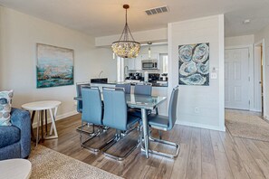 A modern kitchen with stainless steel appliances, a dining area with a glass table and chairs, and a large abstract painting on the wall. - Delightful Beach Getaway with Water Views, Beach Access, Deck & Fast WiFi (Santa Rosa Beach)