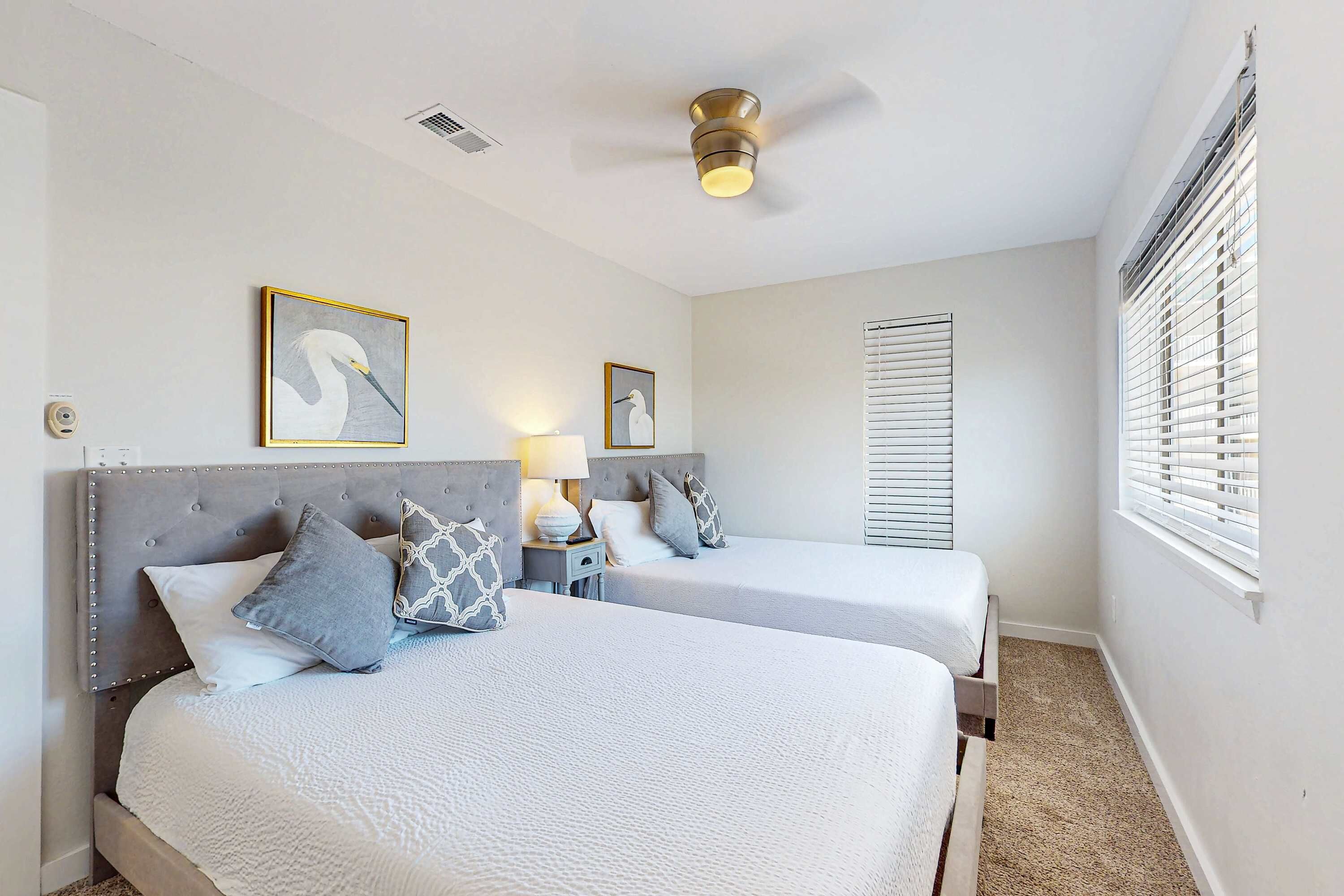A hotel room with two beds, a ceiling fan, and a window with blinds.