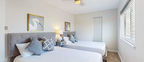 A hotel room with two beds, a ceiling fan, and a window with blinds.