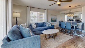 Ein modernes Wohnzimmer mit einer blauen Sofagarnitur, einem runden Couchtisch und einem Essbereich mit einem Glastisch und blauen Stühlen.