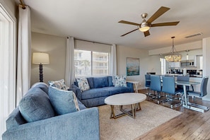 A modern living room with a blue sofa set, a round coffee table, and a dining area with a glass table and blue chairs. - Delightful Beach Getaway with Water Views, Beach Access, Deck & Fast WiFi (Santa Rosa Beach)