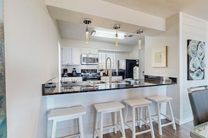 A modern kitchen with white cabinetry, a central island with bar stools, stainless steel appliances, and pendant lighting. - Delightful Beach Getaway with Water Views, Beach Access, Deck & Fast WiFi (Santa Rosa Beach)