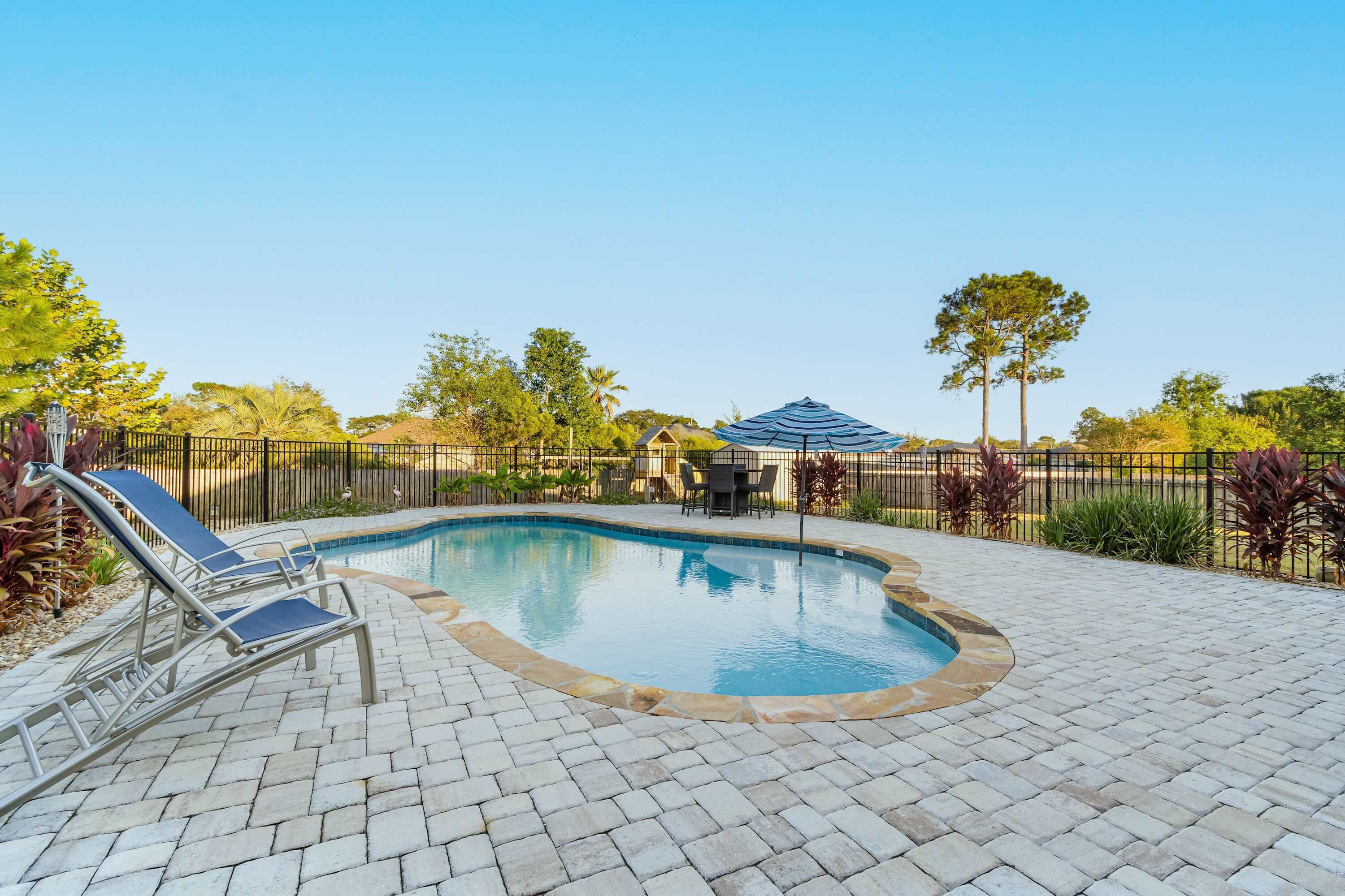 Una piscina con poltrona relax, un'area salotto coperta e un patio recintato.