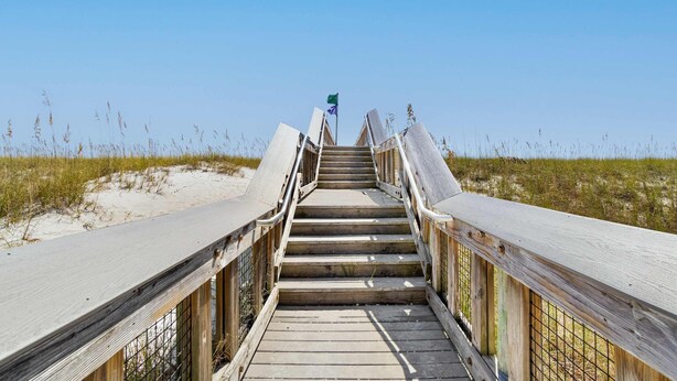 Una passerella in legno che conduce a una spiaggia con dune sabbiose e vegetazione rada.