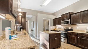 Una cucina moderna con mobili in legno scuro, piani in granito, elettrodomestici in acciaio inossidabile e illuminazione sotto i pensili.