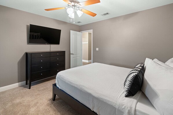 A bedroom with a bed, a dresser, a ceiling fan, and a TV mounted on the wall. - Single-level home with pool, enclosed yard, screened lanai, grill & home office (Navarre)