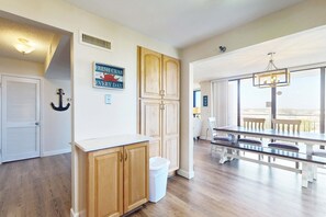 A kitchen with wooden cabinets, a white countertop, and a view of the dining area with a bench and table. - Warm, welcoming condo with outdoor pool & clubhouse - short stroll to beach (Destin)