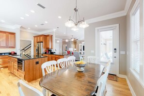 Una cocina moderna con armarios de madera, una isla central y una zona de comedor con mesa de madera y sillas blancas.