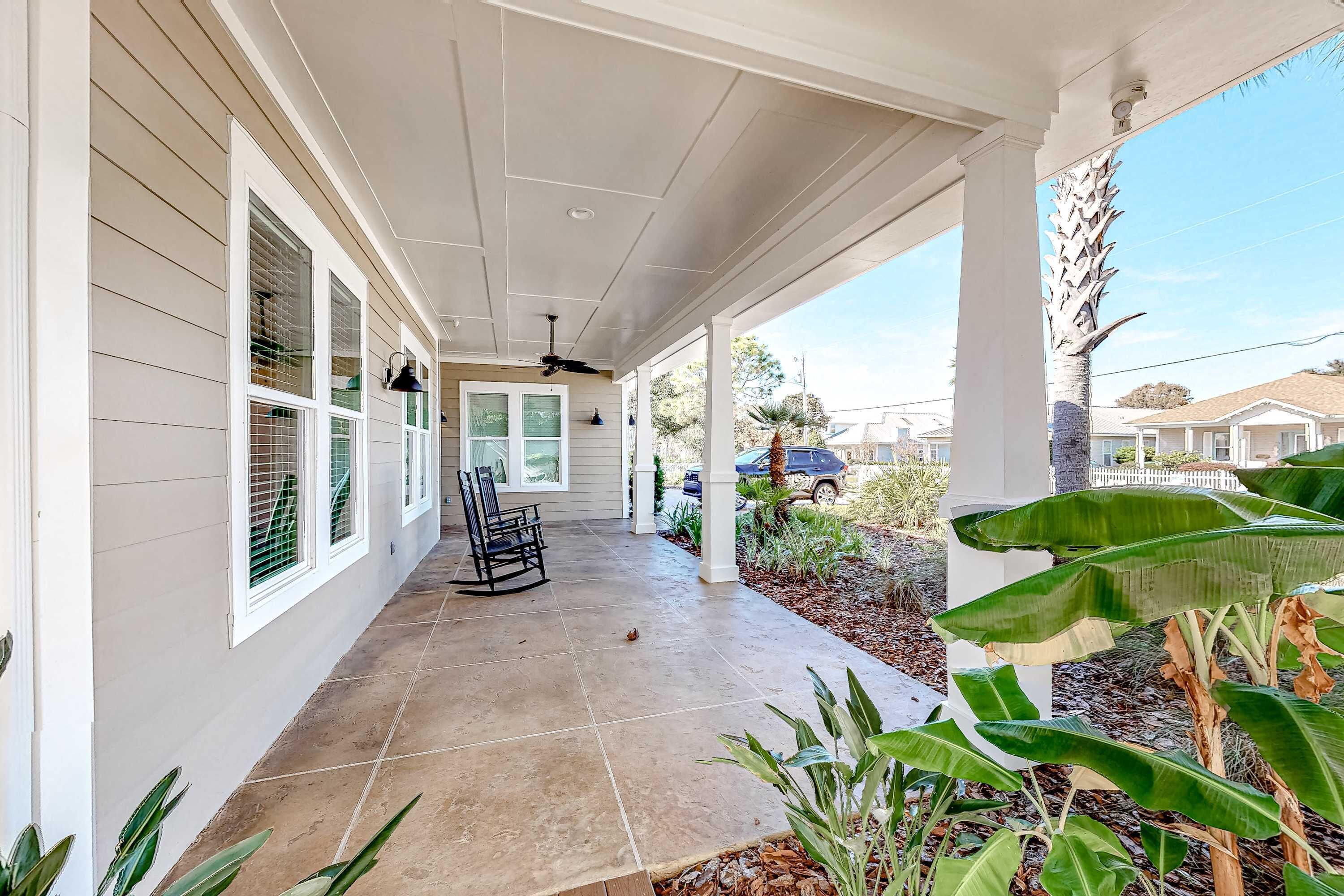 A covered porch with a tiled floor, a rocking chair, and a view of a residential neighborhood.