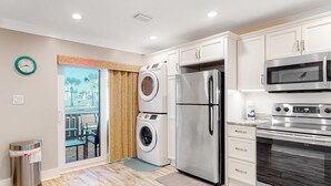 Eine moderne Küche mit Edelstahlgeräten, darunter ein Kühlschrank, eine Mikrowelle und ein Backofen. Eine Waschmaschine und ein Mülleimer sind ebenfalls zu sehen.