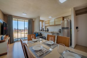 Eine moderne Küche mit einem großen Kühlschrank, ein Essbereich mit Tisch für vier Personen und Blick auf die Stadt durch große Fenster.