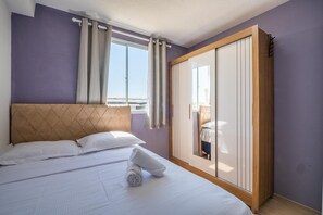 A bedroom with a bed, a wardrobe, a window with curtains, and a view of the sea. - Mirante-506 - Apt 300m From the Beach by Carpediem (Fortaleza)
