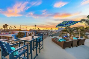 Um terraço no telhado com uma mesa, cadeiras, um sofá de vime e um guarda-sol.