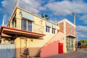 Um edifício de dois andares com uma porta vermelha, uma escadaria e uma cerca de metal.