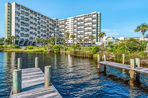 A multi-story hotel with balconies, a dock extending into a body of water, and surrounding greenery. - Beachfront condo in gated resort with pools, lake access, fast WiFi & patio (Panama City Beach)