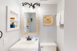A bathroom with a white sink, a mirror, a towel rack, and a framed picture on the wall. - Beachfront condo in gated resort with pools, lake access, fast WiFi & patio (Panama City Beach)