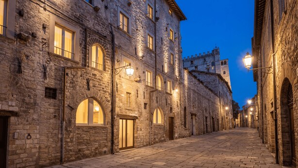Un edificio de piedra con ventanas de arco y una torre, iluminado por farolas.