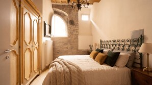 Un dormitorio con cama, armario de madera, pared de piedra y una araña.
