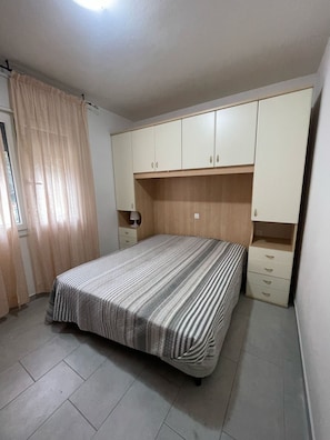 A bedroom with a bed, a nightstand, a wardrobe, and a window with curtains. - Cozy Flat at a Short Distance From Rosolina Beach (Rosolina)