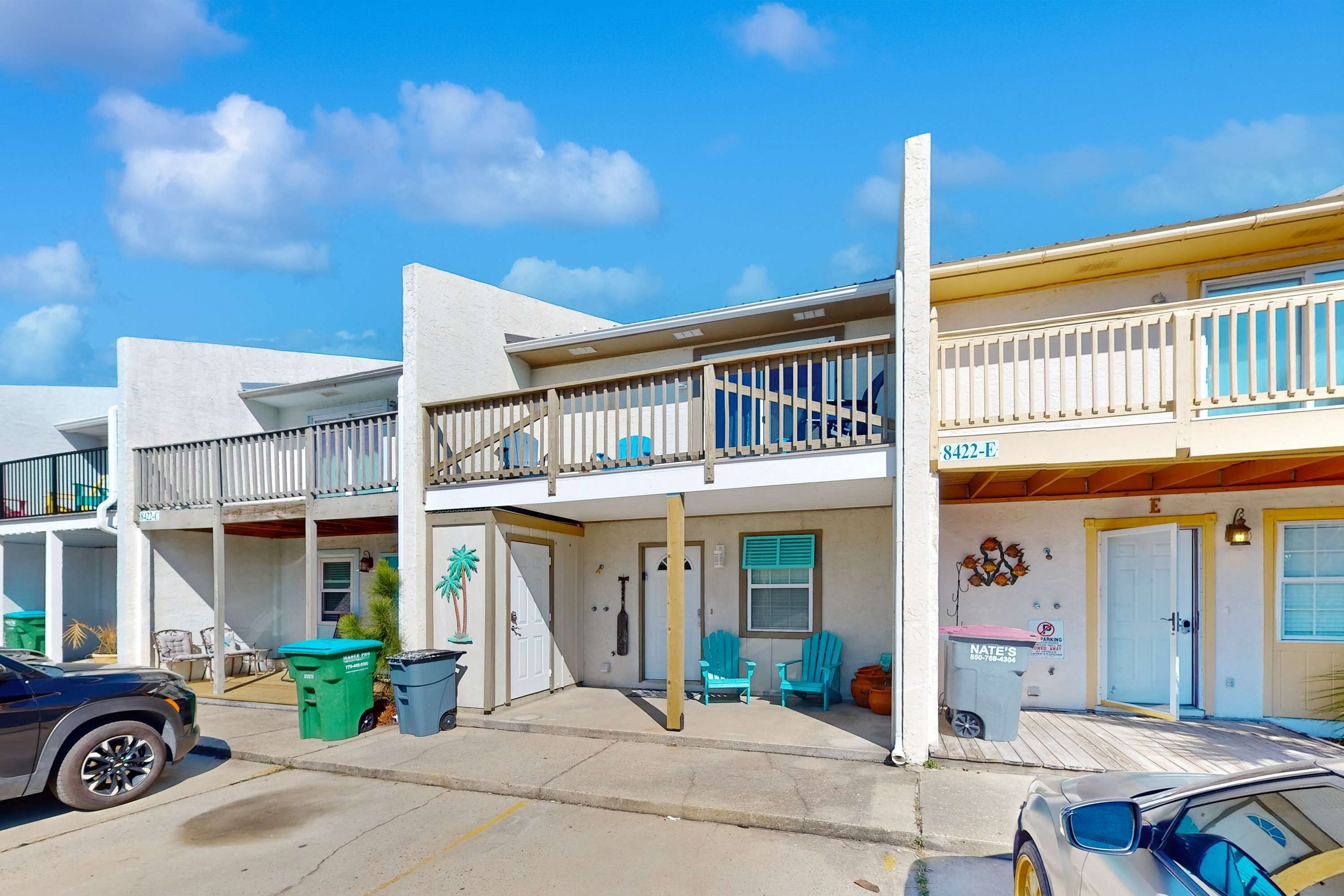 A two-story building with a balcony, a parking area, and a door marked with a number.