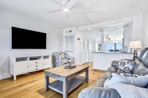 Ett modernt vardagsrum med ett soffbord i trä, en grå soffa med mönstrade kuddar, en vit TV-möbel och en takfläkt.