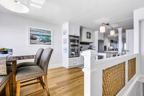 Eine moderne Küche mit weißen Schränken, ein Essbereich mit einem Holztisch und Stühlen sowie Blick auf das Wohnzimmer.