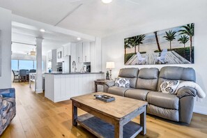 Ett modernt vardagsrum med en soffa i läder, ett soffbord i trä och en tavla som föreställer en strandscen.
