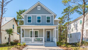 A two-story house with a front porch, a small front yard, and a clear blue sky. - Lovely Two-Story Home with Porches, Access to Pool & Dock (Inlet Beach)