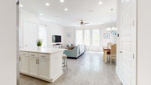 A spacious living room with a sofa, TV, and dining area. - Lovely Two-Story Home with Porches, Access to Pool & Dock (Inlet Beach)