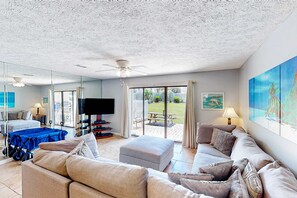 A spacious living room with a large couch, a flat-screen TV, and a ceiling fan. - Gulf Highland | Townhouse in Panama City Beach with on-site mini golf & pool (Panama City Beach)
