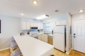 A compact kitchen with white cabinets, a central island with stools, a microwave, stove, sink, and a refrigerator. - Gulf Highland | Townhouse in Panama City Beach with on-site mini golf & pool (Panama City Beach)