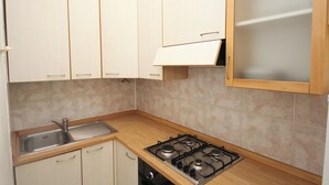 A kitchen with white cabinets, a stainless steel sink, and a gas stove. - Rosolina Mare Flat Near Beach (Rosolina)