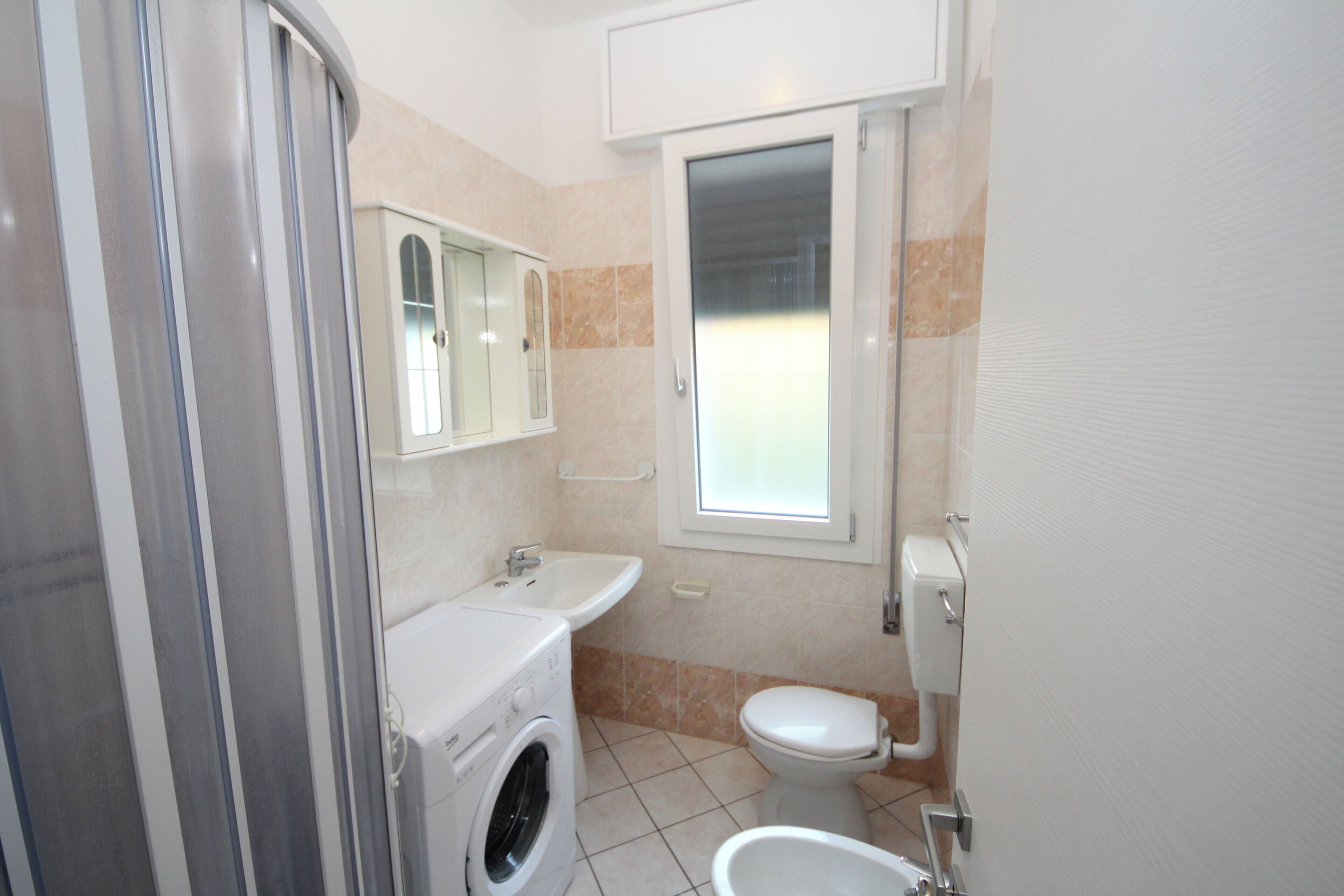 Une petite salle de bain équipée d’un lave-linge, d’un évier et de toilettes.