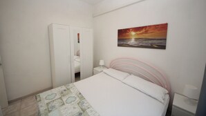 A bedroom with a bed, a nightstand, a wardrobe, and a painting of a sunset over the ocean. - Rosolina Mare Flat Near Beach (Rosolina)