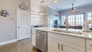 A modern kitchen with white cabinetry, stainless steel appliances, pendant lighting, and a view to the living area. - Elegant condo with 2 community pools, hot tub, & beach access across the road (Seacrest)