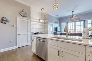 Een moderne keuken met witte kastjes, roestvrijstalen apparatuur, hangende lampen en uitzicht op de woonkamer.