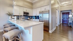 A modern kitchen with white cabinetry, stainless steel appliances, and a large island with bar stools. - Elegant condo with 2 community pools, hot tub, & beach access across the road (Seacrest)