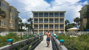 A man walking on a wooden boardwalk with a large hotel building in the background. - Elegant condo with 2 community pools, hot tub, & beach access across the road (Seacrest)