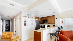 A modern kitchen with white cabinetry, a central island, and a dining area with wicker chairs. - Stunning Florida getaway with Gulf view, pools, & central location (Panama City Beach)