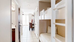 A narrow hallway with a bunk bed on the right, a door leading to a room, and a dining area in the background. - Stunning Florida getaway with Gulf view, pools, & central location (Panama City Beach)