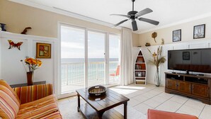 A living room with a sofa, a coffee table, a TV, and a balcony with a view. - Stunning Florida getaway with Gulf view, pools, & central location (Panama City Beach)