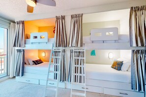 Ein Mehrbettzimmer mit Etagenbetten, Vorhängen, einer Treppe und einer kleinen Schreibtischzeile.
