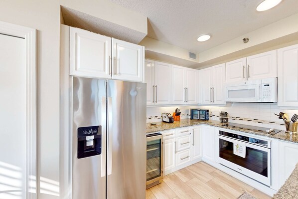 A modern kitchen with white cabinetry, stainless steel appliances, and a granite countertop. - Beachfront condo with balcony, beach & pool views, pool, tennis, gym, W&D, & AC (Navarre Beach)